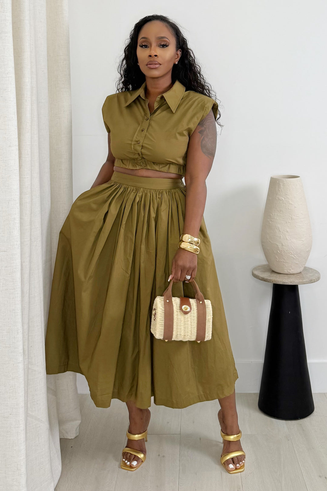 Woman in a green outfit holding a handbag indoors.